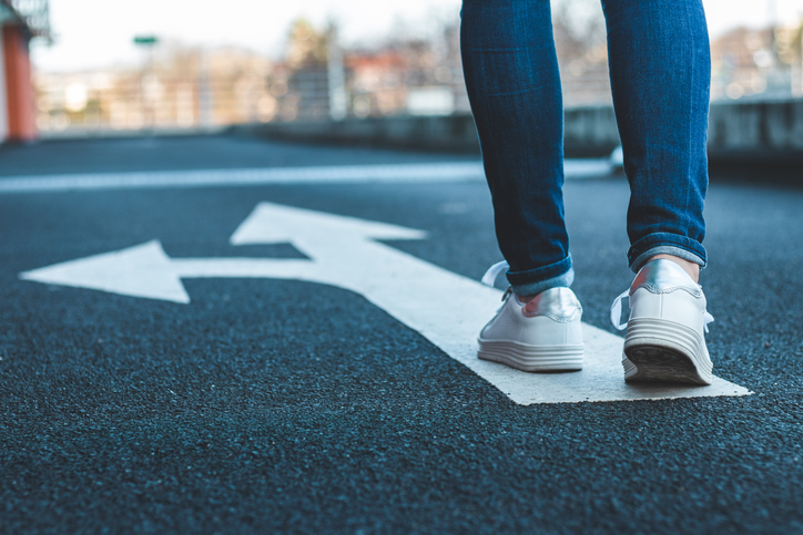 Photo of person making decision which way to go walking on a directional sign on an asphalt road