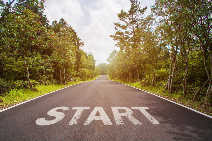 The word "Start" painted on a sunlit highway with trees on either side